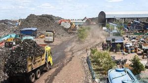 A large open-air waste dump yard or landfill site featuring heavy machinery and dump trucks.