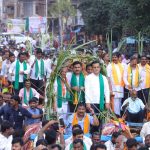 Political leaders and party workers participating in a crowded roadshow or rally with sugarcane decorations.