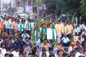 Political leaders and party workers participating in a crowded roadshow or rally with sugarcane decorations.