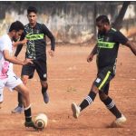 Players competing in an intense football match on a dirt field.